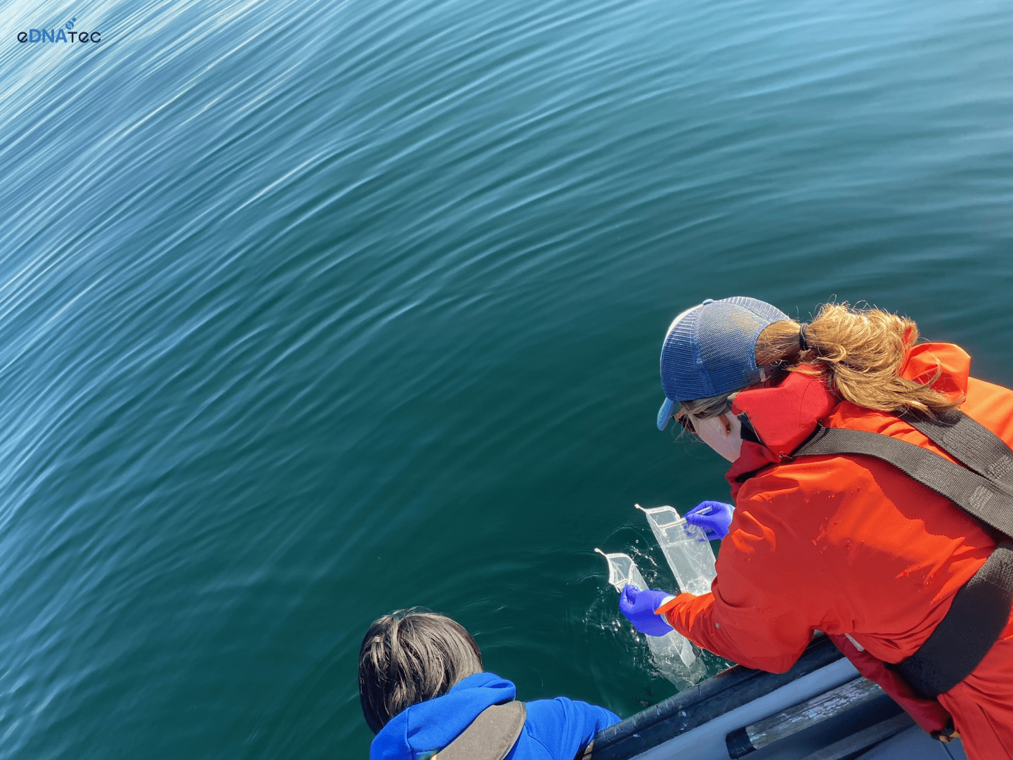 Two eDNAtec staff members are aboard a boat, collecting water samples from the Atlantic Ocean.
