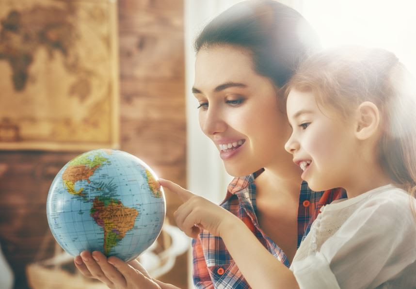 A woman looking at a globe with a female child.