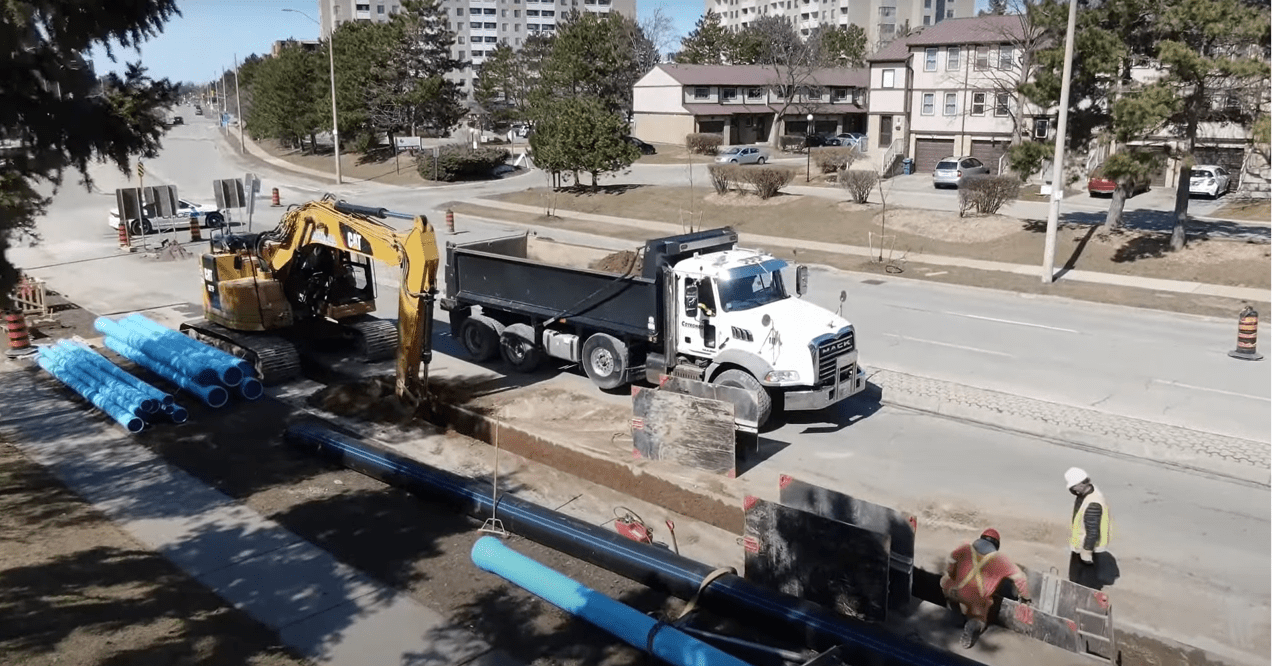 Peel Region water utility field workers replacing a watermain on the side of the road with large pipes and equipment.