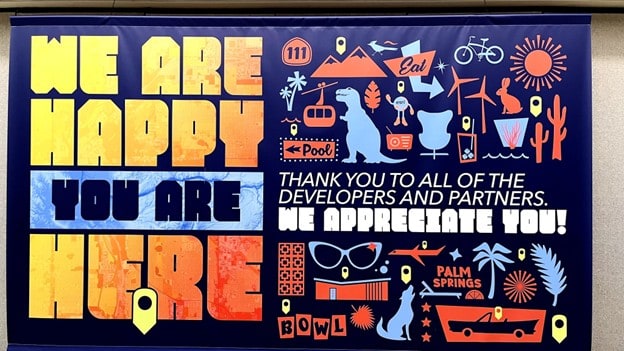 A banner that says, in bright yellow and orange letters against a dark blue backdrop, “We are happy you are here – thank you to all of the developers and partners. We appreciate you!” Surrounding the words are various vintage-inspired icons representing Palm Springs, California.