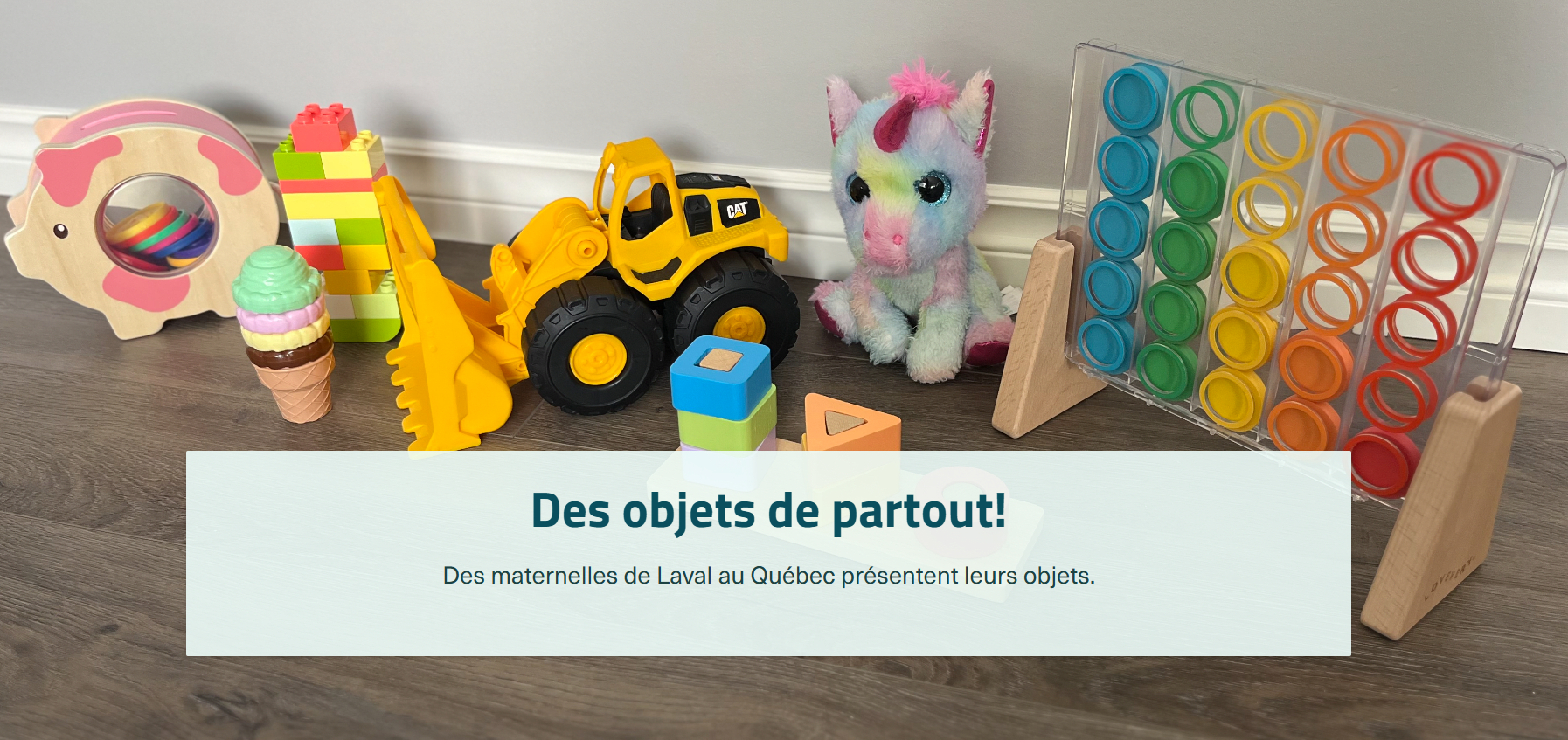 A range of children's toys are lined up on the floor. From left to right, there is a small wooden pig with colored pieces. The section where the pieces are located is closed by two transparent plastic pieces. Next to the pig is a tower made of LEGO-style blocks and a plastic cone with four balls stacked on top of each other. One is green, another is pink, then there is a beige one and a brown one. To the right of these toys is a small tractor with a bulldozer-type mechanical shovel. To its right is a multicoloured stuffed unicorn with pink mane, horn, inner ears and underside of the legs. In front of the unicorn is a set of wooden blocks that are stacked on three small pegs of different shapes: a square, a triangle and a circle. To the right of these toys is a game on a stand with colored discs arranged in five columns in the colours blue, green, yellow, orange and red. The blue column has five discs, while the green column has four, the yellow column has three, the orange column has two, and the red column has one. Centred at the bottom of the image is a box with the title and subtitle: “Des objets de partout! Des maternelles de Laval au Québec présentent leurs objets” (“Objects from all over! Preschoolers from Laval, Québec display their objects”).