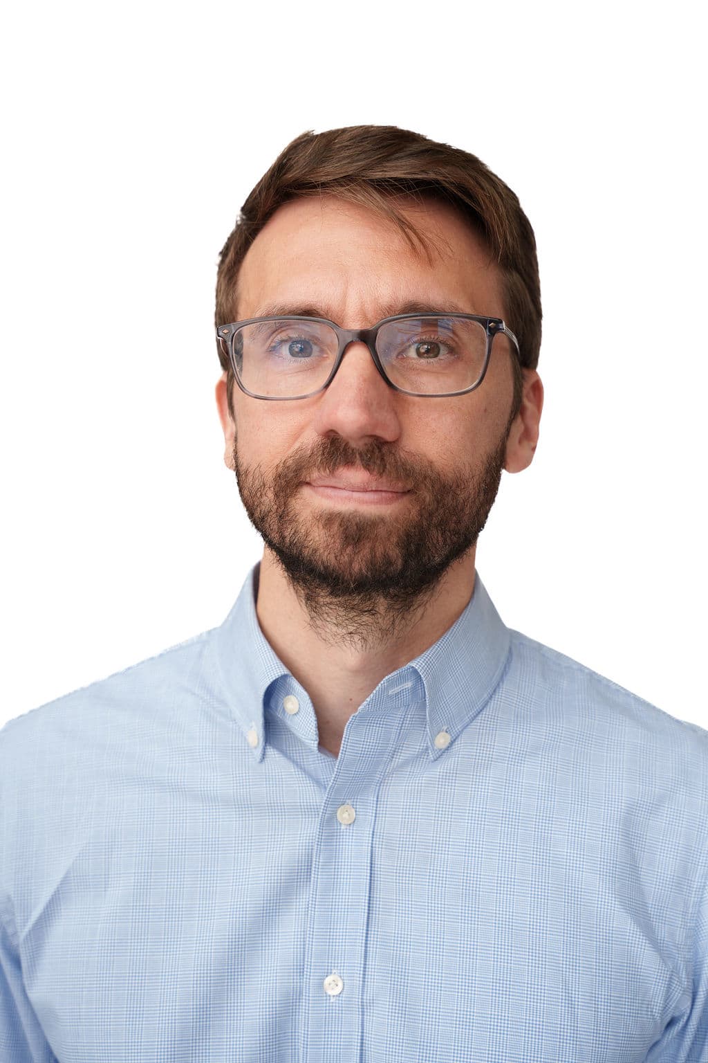 Headshot of a Caucasian man on a white background. He has short light brown hair and brown eyes. He is wearing large rectangular eyeglasses. He has a faint smile and a brown beard. He is wearing a plain light blue shirt with white buttons.