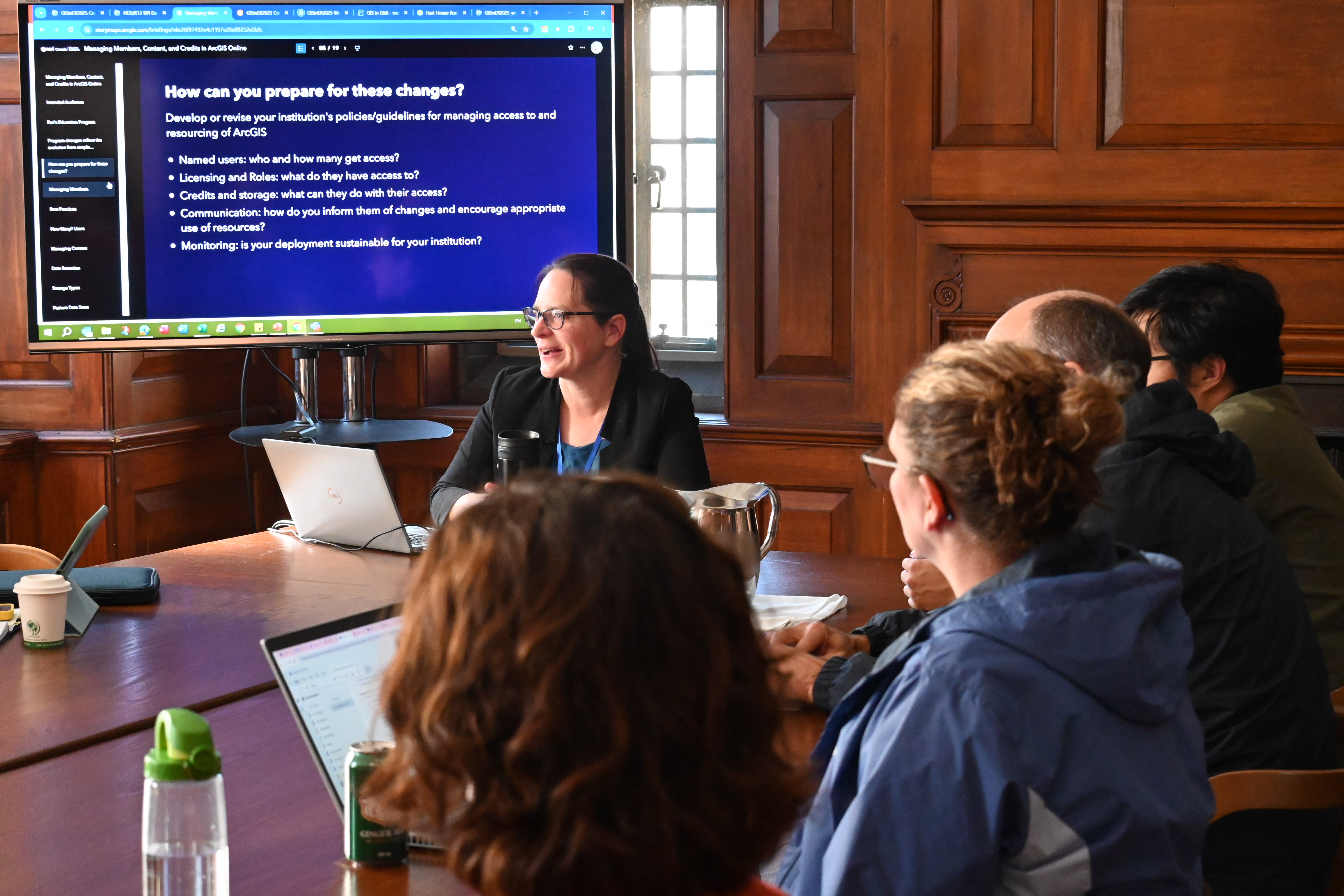 A woman leading a discussion with a group of people with a screen behind her.