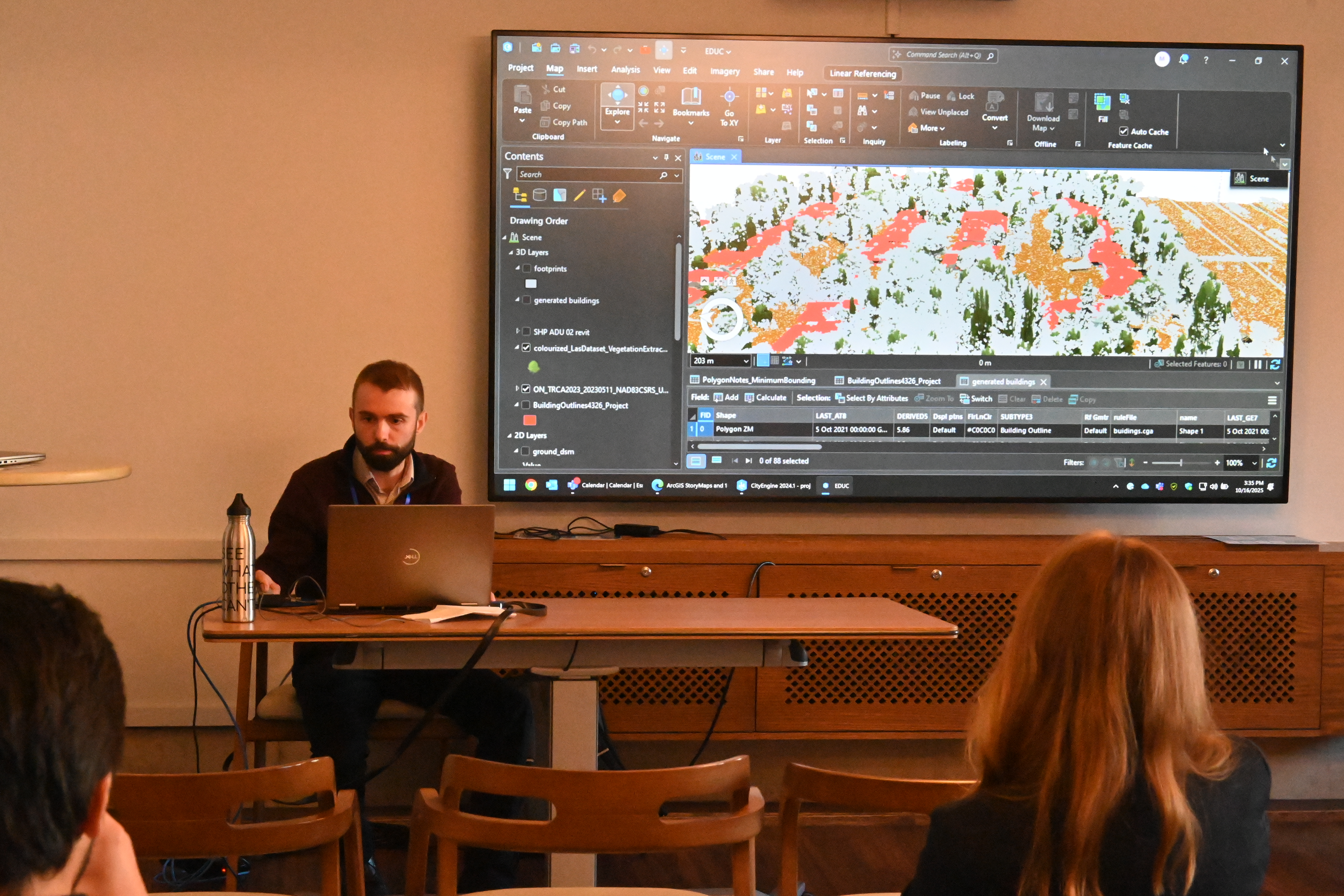 A man sitting in front of a screen demonstrating how to do something in a classroom.