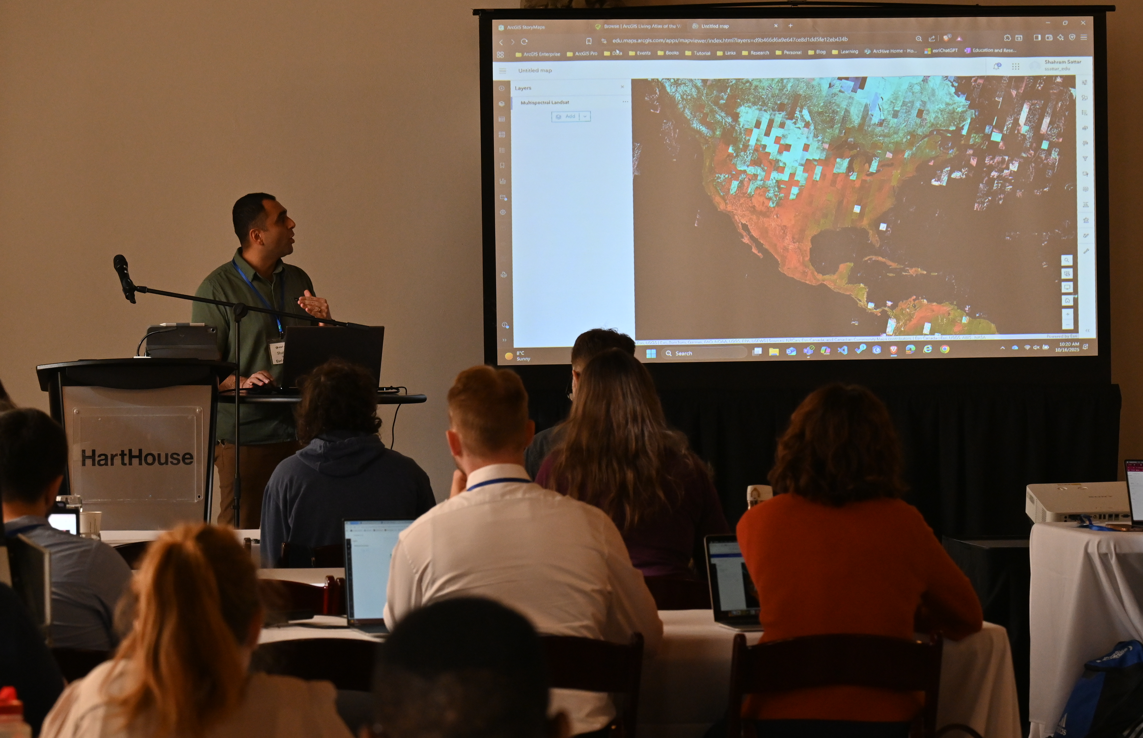 A man at the front of a room of people presenting about content on the screen.