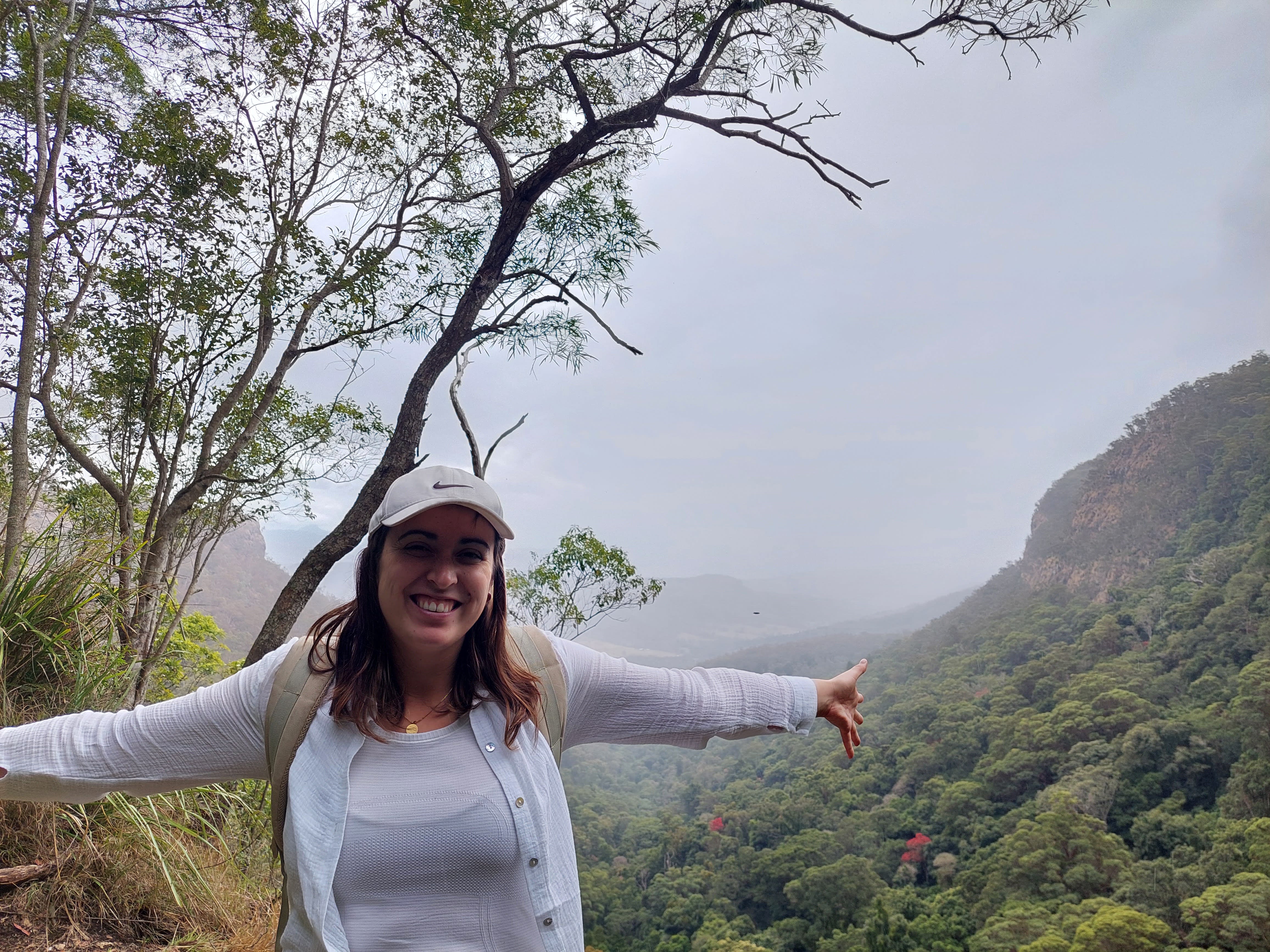 Une femme souriant, les bras ouverts, devant un panorama forestier.