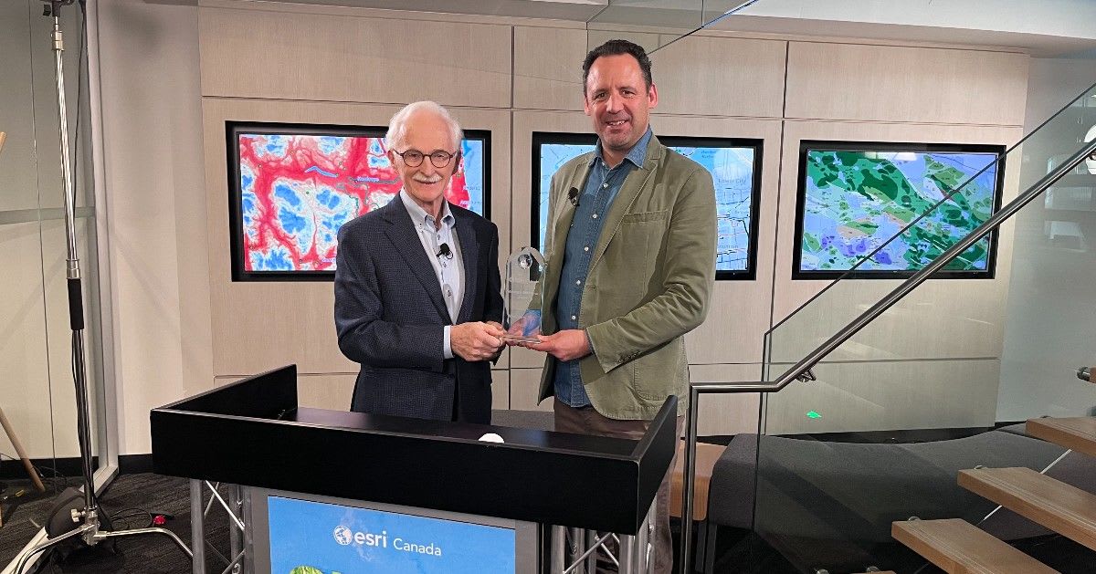 Two men standing at a podium, smiling at the camera while both holding a glass award.