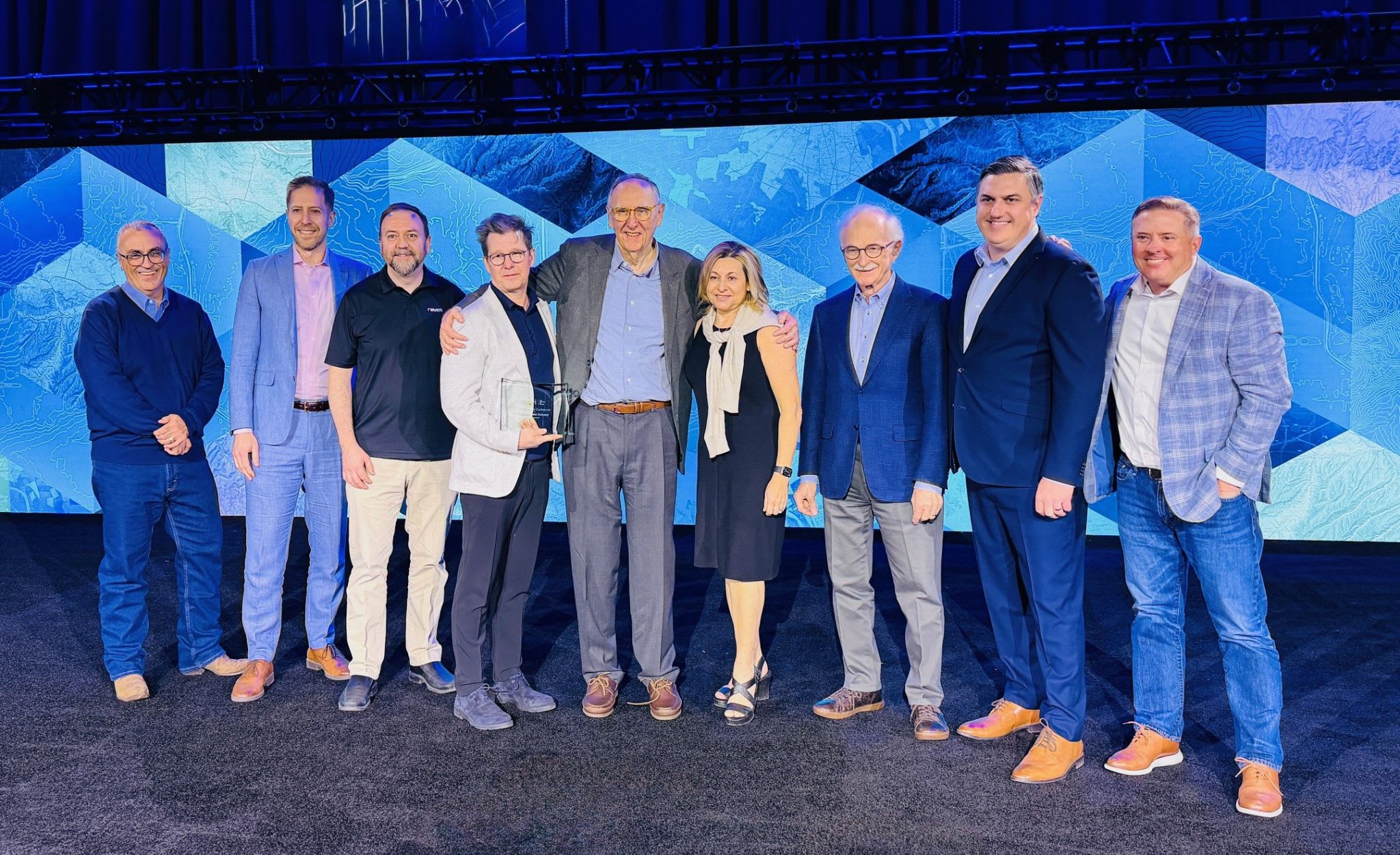 Des membres de l&rsquo;&eacute;quipe de Raven Connected posent sur sc&egrave;ne aux c&ocirc;t&eacute;s de dirigeants d&rsquo;Esri et d&rsquo;Esri Canada lors de la c&eacute;r&eacute;monie de remise de prix tenue dans le cadre de la Conf&eacute;rence des partenaires d&rsquo;Esri 2026, devant un d&eacute;cor g&eacute;om&eacute;trique bleu.