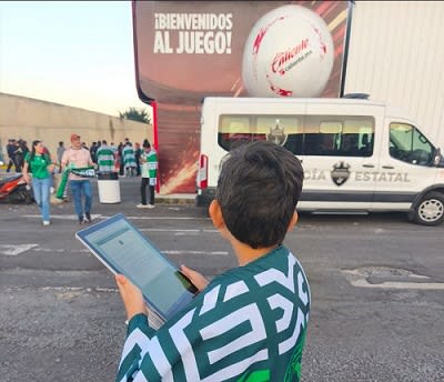 A young person standing outside a stadium collecting data on a tablet.