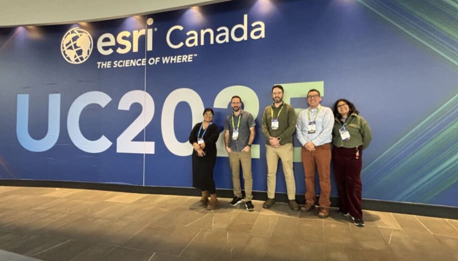 Five members of the Cree Nation Government&rsquo;s GIS program team stand smiling before a large blue Esri Canada UC2025 conference wall in Toronto.