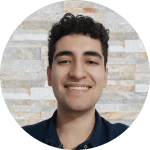 Oscar Andrade-Rios, a man with light skin, short dark curly hair and a navy collared shirt, smiles against a brick background.