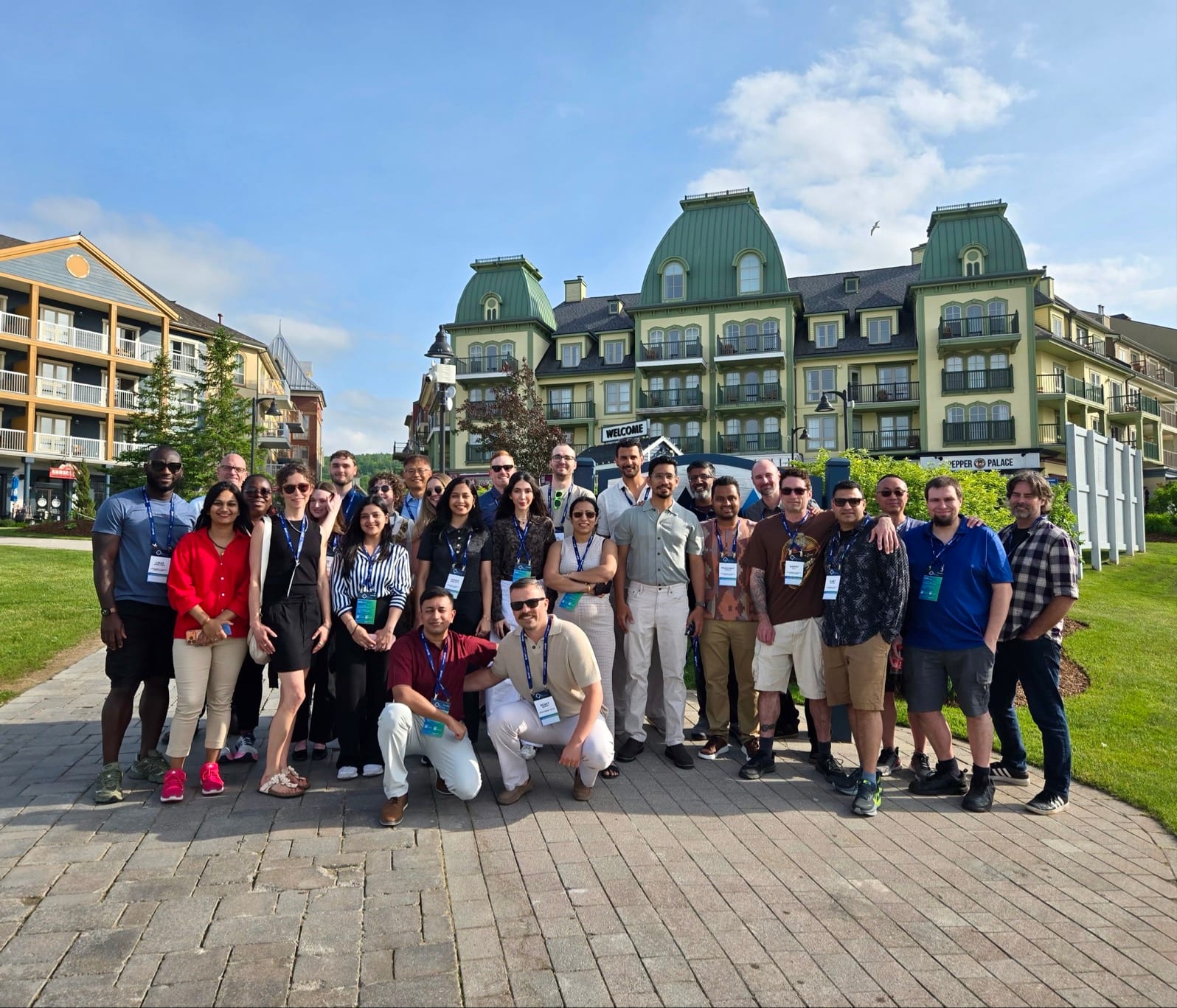 Devant plusieurs bâtiments pittoresques d’un complexe hôtelier et sous un ciel bleu, vingt-huit membres de l’équipe des Services d’évaluation d’Esri Canada posent pour la caméra. La plupart portent un insigne de conférence indiquant leur participation à la conférence des employés Inspire 2026 de l’entreprise.