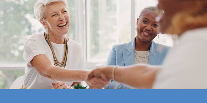 Smiling woman shakes person's hand while woman sitting next to her smiles.