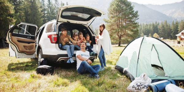 family sitting in back of car and setting up campsite