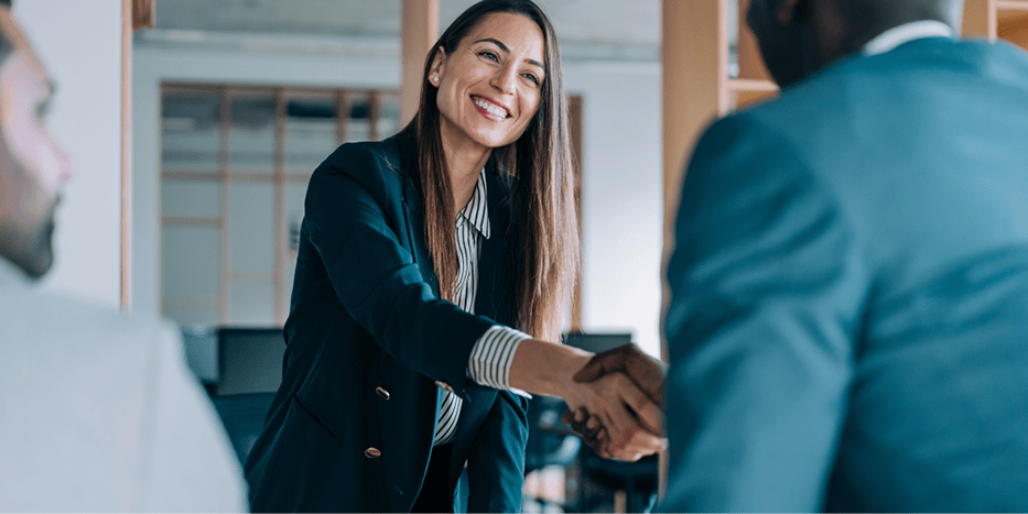 Professionally dressed woman shaking hands over a meeting table