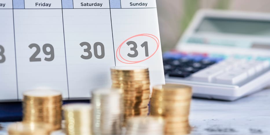 Coins on a table in front of the bottom portion of a calendar with a Sunday the 31st date circled in red marker.