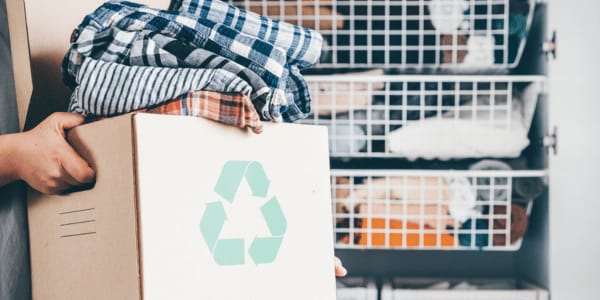 person holding recycling box when cleaning out closet to make capsule wardrobe