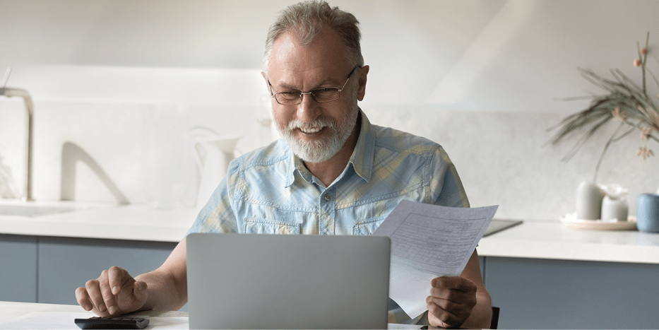 Man smiling looking at a laptop with form in hand