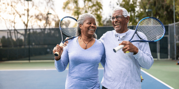 couple holding tennis rackets walking on tennis court