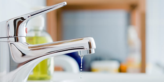 Dripping faucet with soap and other products nearby in the background.