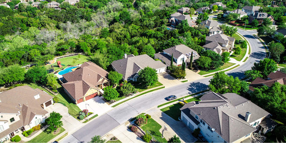 Aerial view of suburban neighborhood filled with large homes, trees, and a winding road. 
