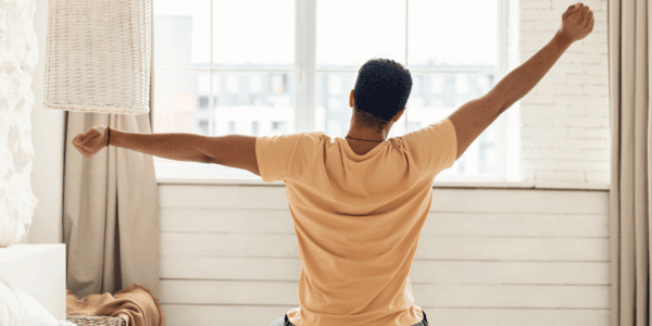 man sitting on bed and stretching his arms in the morning