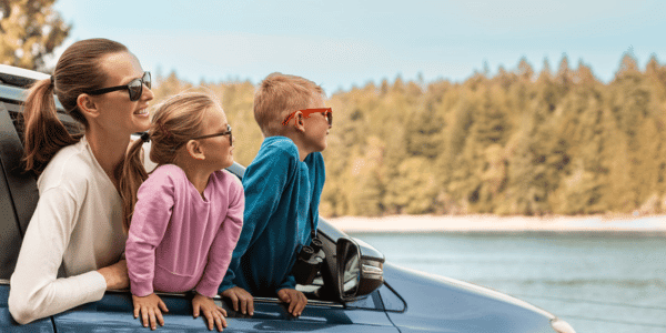 mother and two children looking out car window on road trip