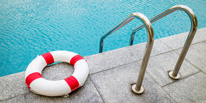 A lifeguard float ring laying on the concrete next to a swimming pool ladder. 