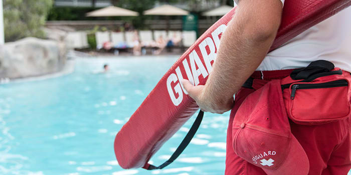 The arm of a lifeguard holding a rescue tube, with their hat and other equipment strapped to their waist.