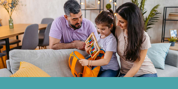 Mom, dad, and daughter on couch as daughter holds backpack and abacus.