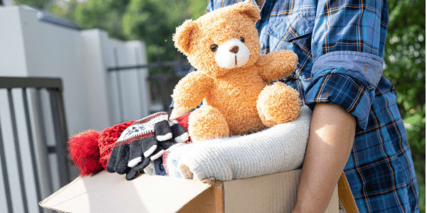 man decluttering for back to school carrying a donation box with teddy bear