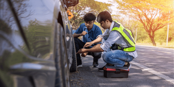 driver and roadside assistance personnel changing tire