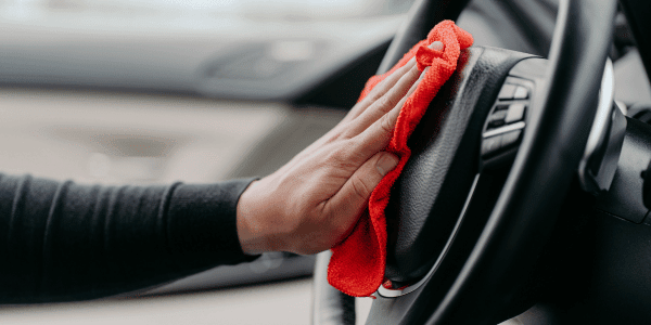person cleaning steering wheel with rag from car supplies kit