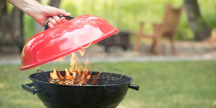Hand putting lid over flaming charcoal grill
