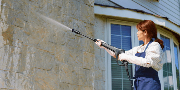 woman pressure washing home exterior