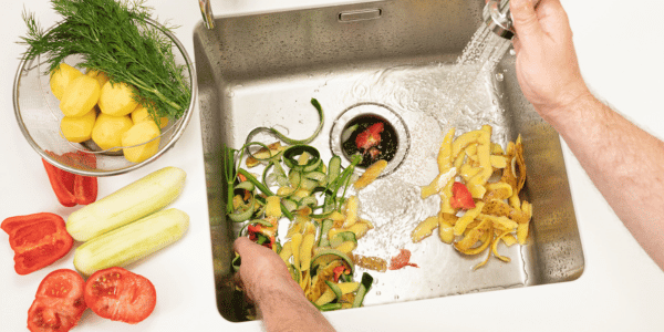 person putting food scraps in garbage disposal