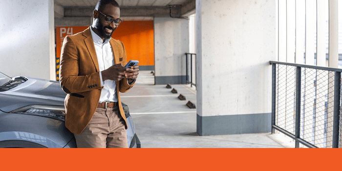 Man texting on a cell phone leans on car in parking garage