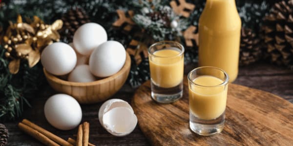two glasses of eggnog next to a basket of eggs