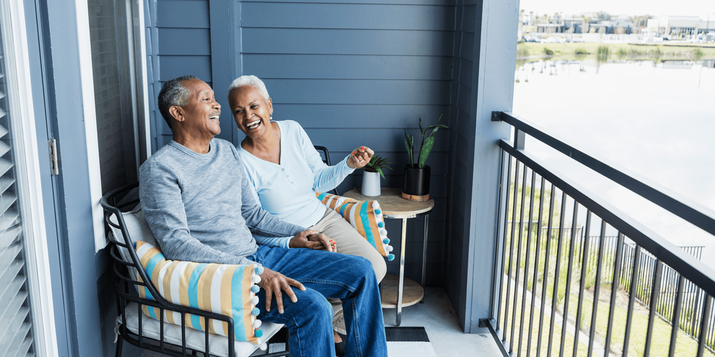 Senior couple relaxing on their porch, holding hands and laughing.