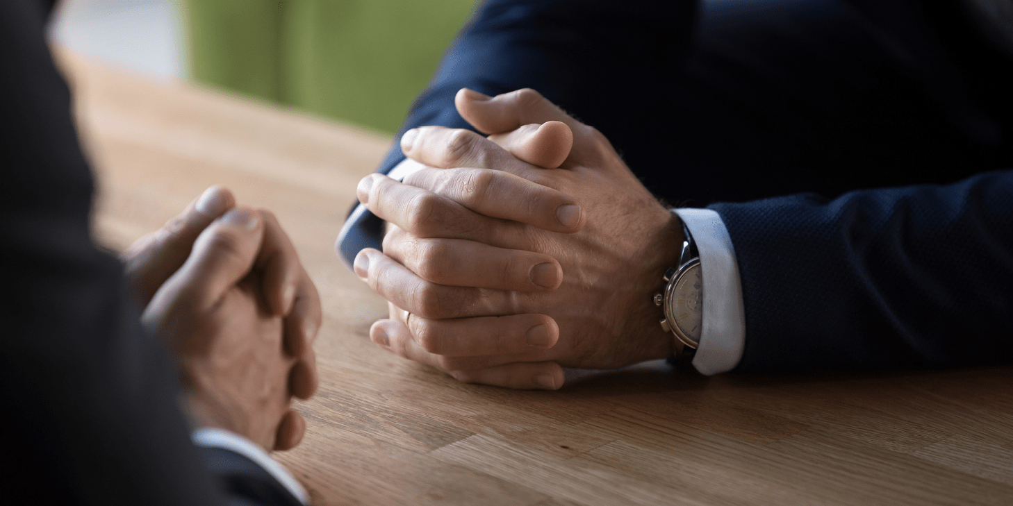 Clasped male hands of two businessmen negotiating at a table.