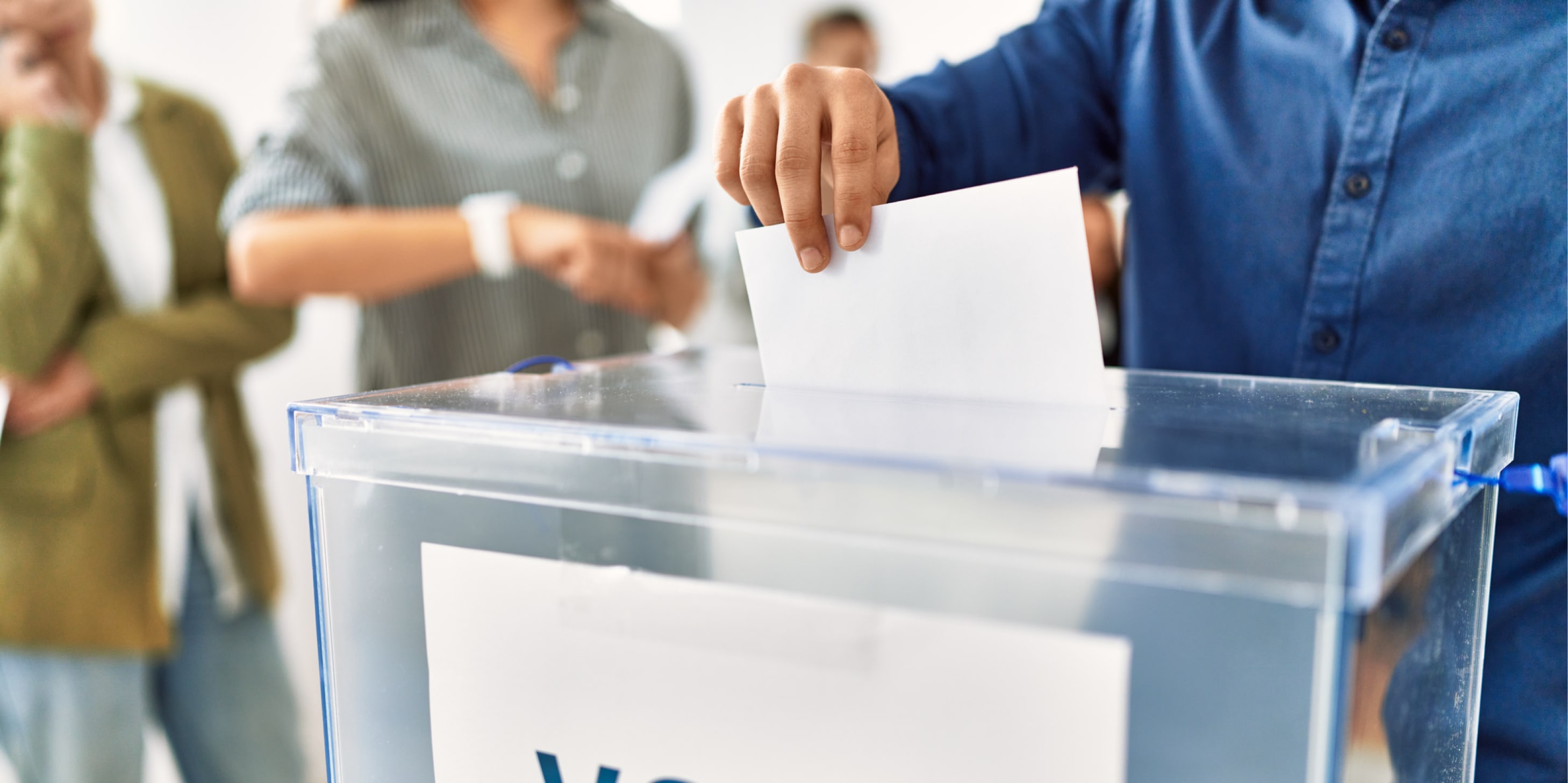 Hand of a man putting a vote in a voting box at an electoral center.