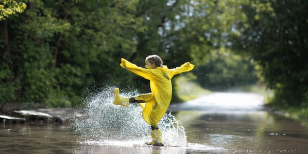 girl wearing yellow rubber boots and a yellow raincoat Jumping in a puddle