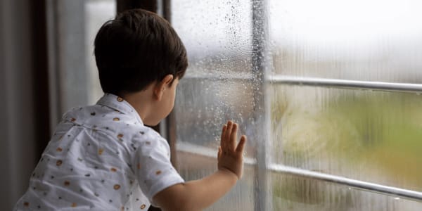 young boy watching the rain through the window