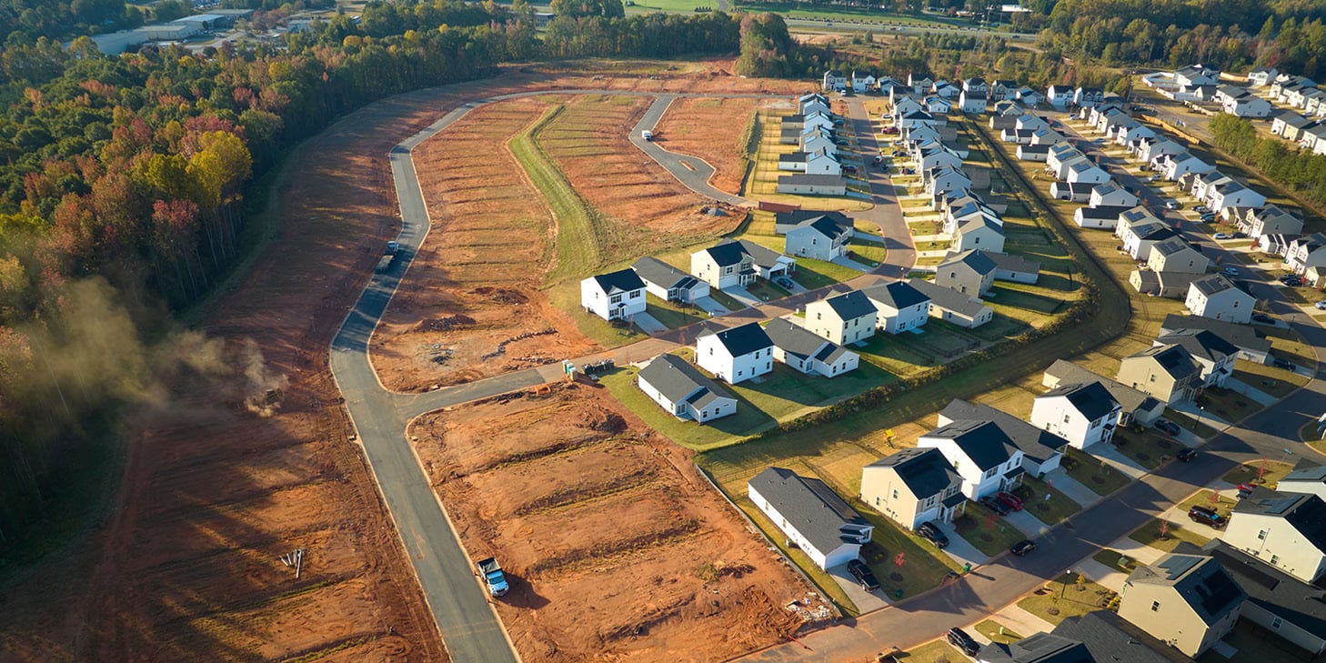 Aerial view of a construction site next to a developed neighborhood of suburban homes