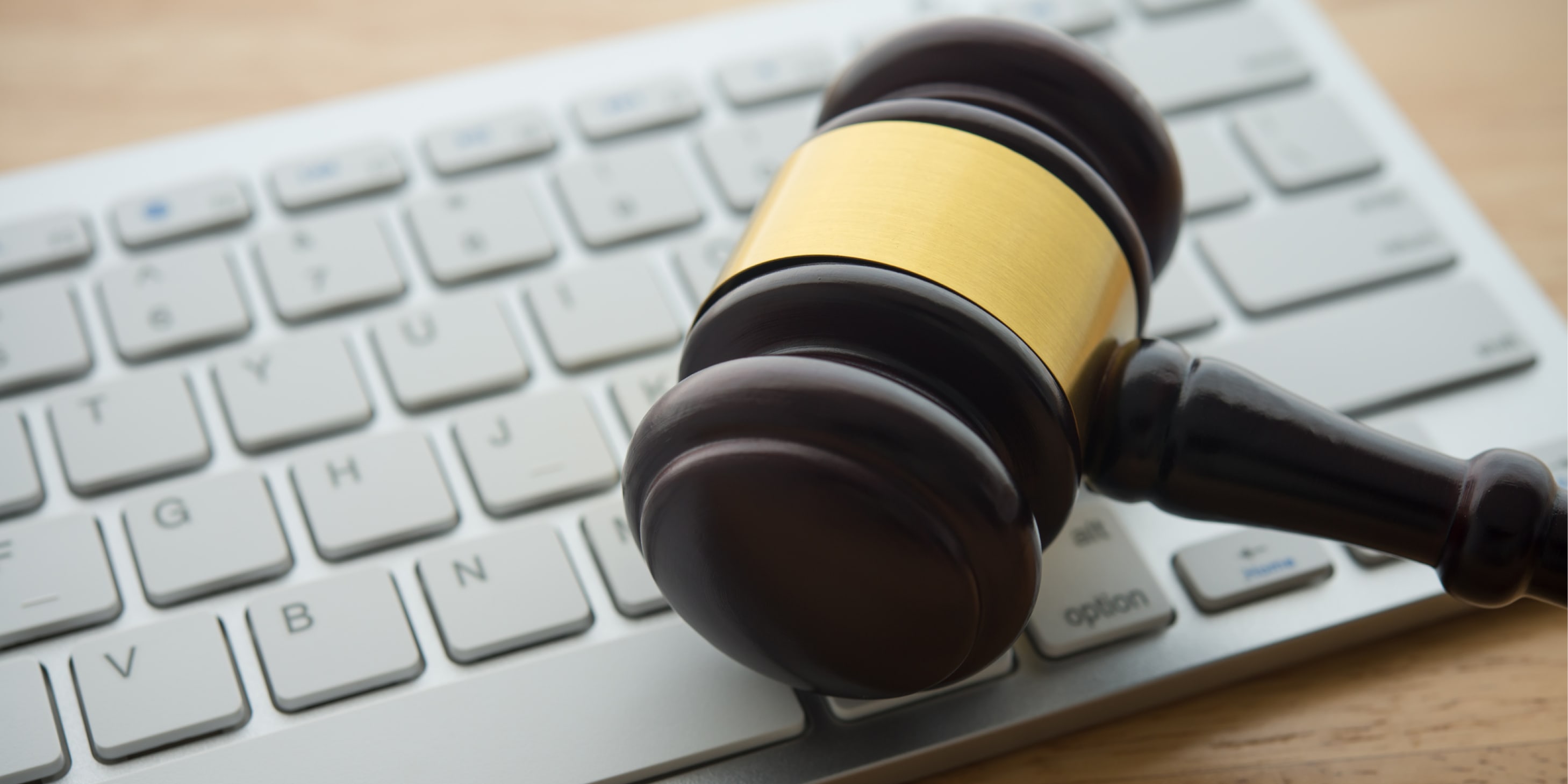 A gavel sitting on a computer keyboard on a wooden desk.