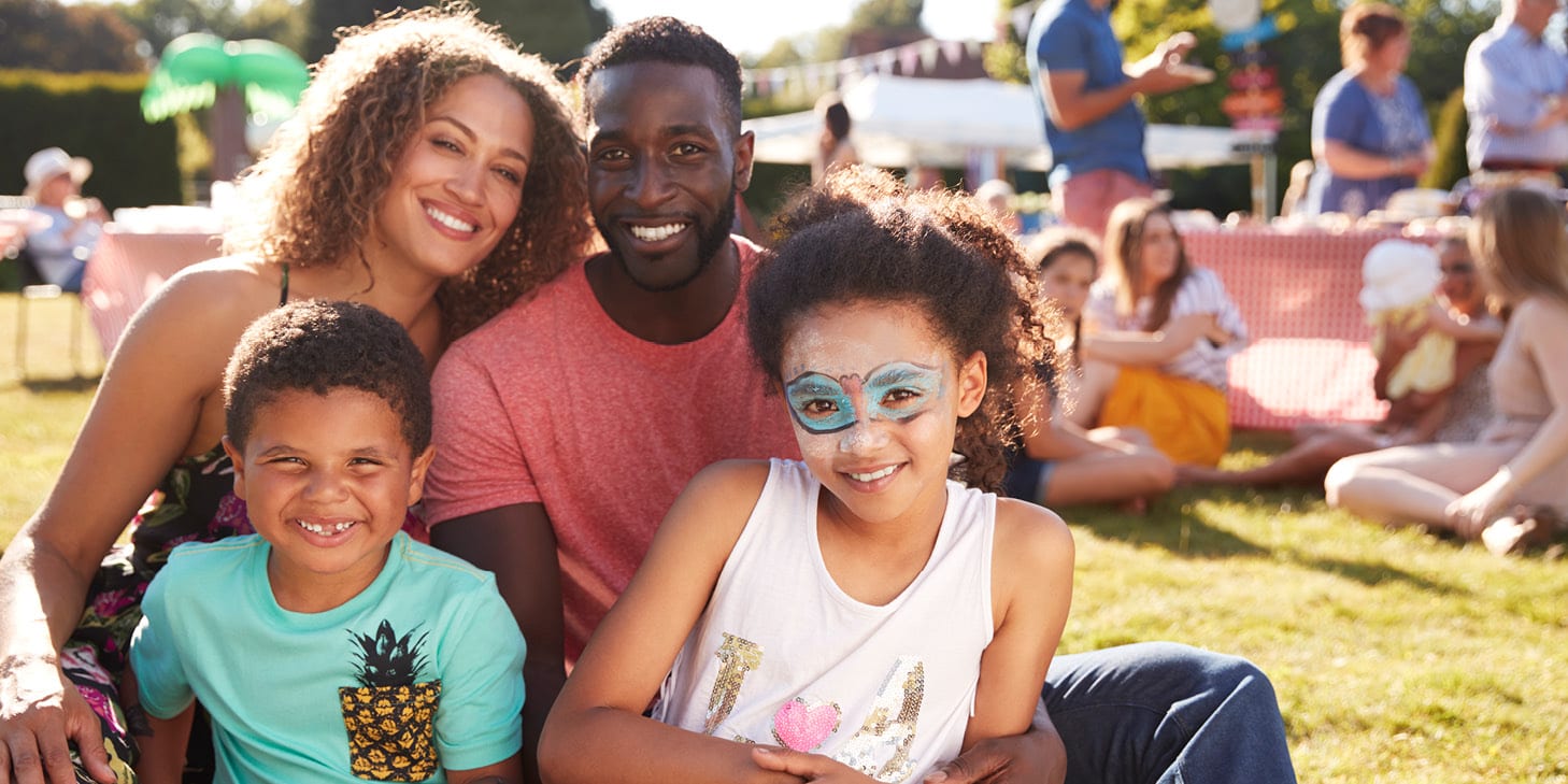A sitting family of four poses for a picture at a summertime event.