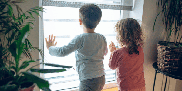 two children looking outside window on rainy day