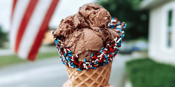 person holding chocolate ice cream in waffle cone with patriotic sprinkles