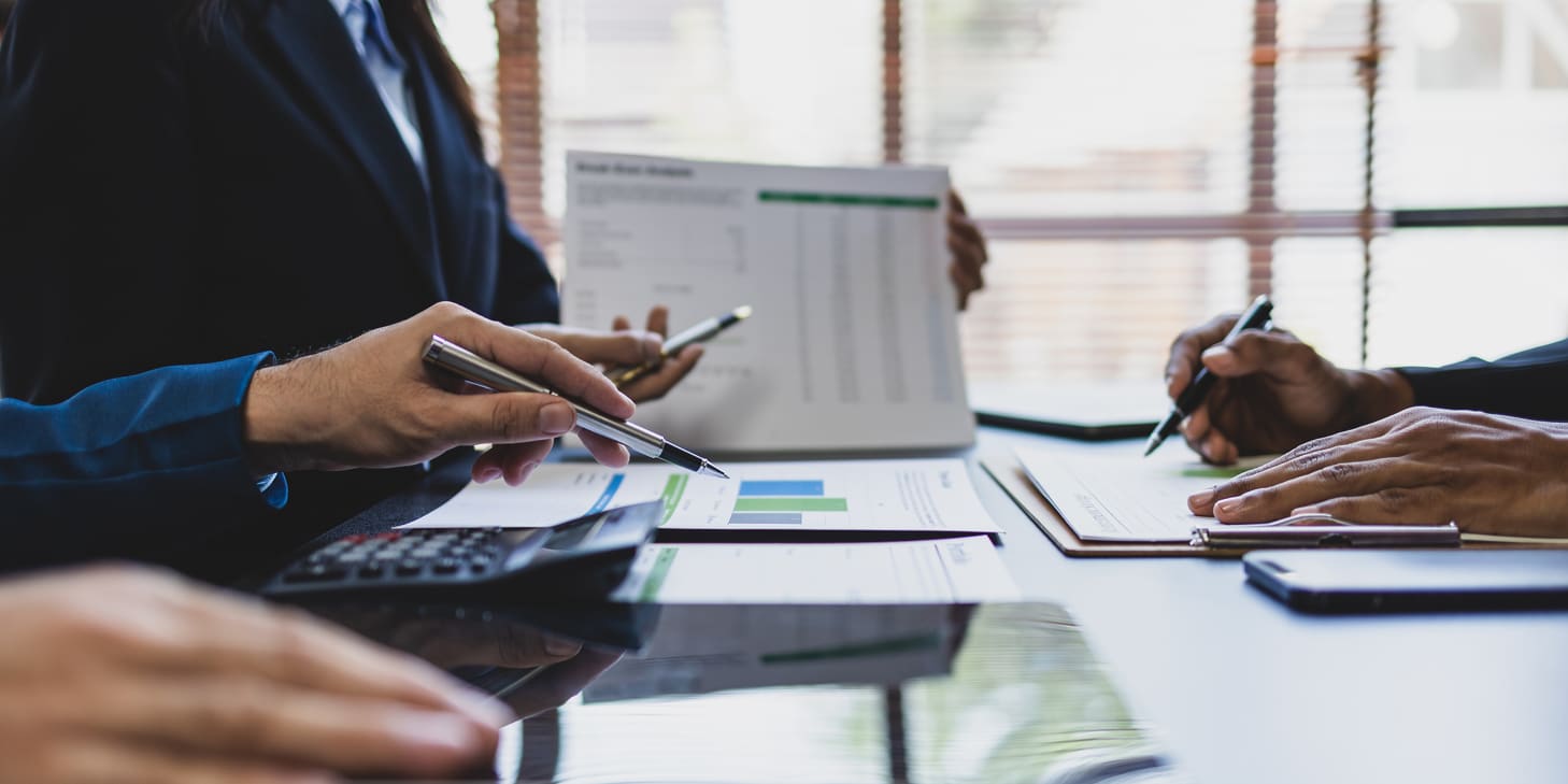 Business meeting with calculators, charts, and graphs sitting on a table.