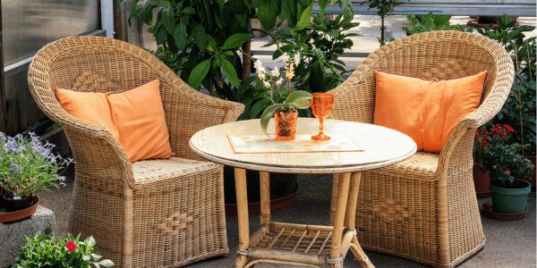 two outdoor wicker dining chairs with table and orange pillows.